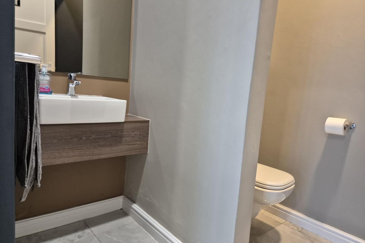 A modern office restroom featuring a wall-mounted vanity with a vessel sink, large mirror, and a private toilet enclosure.