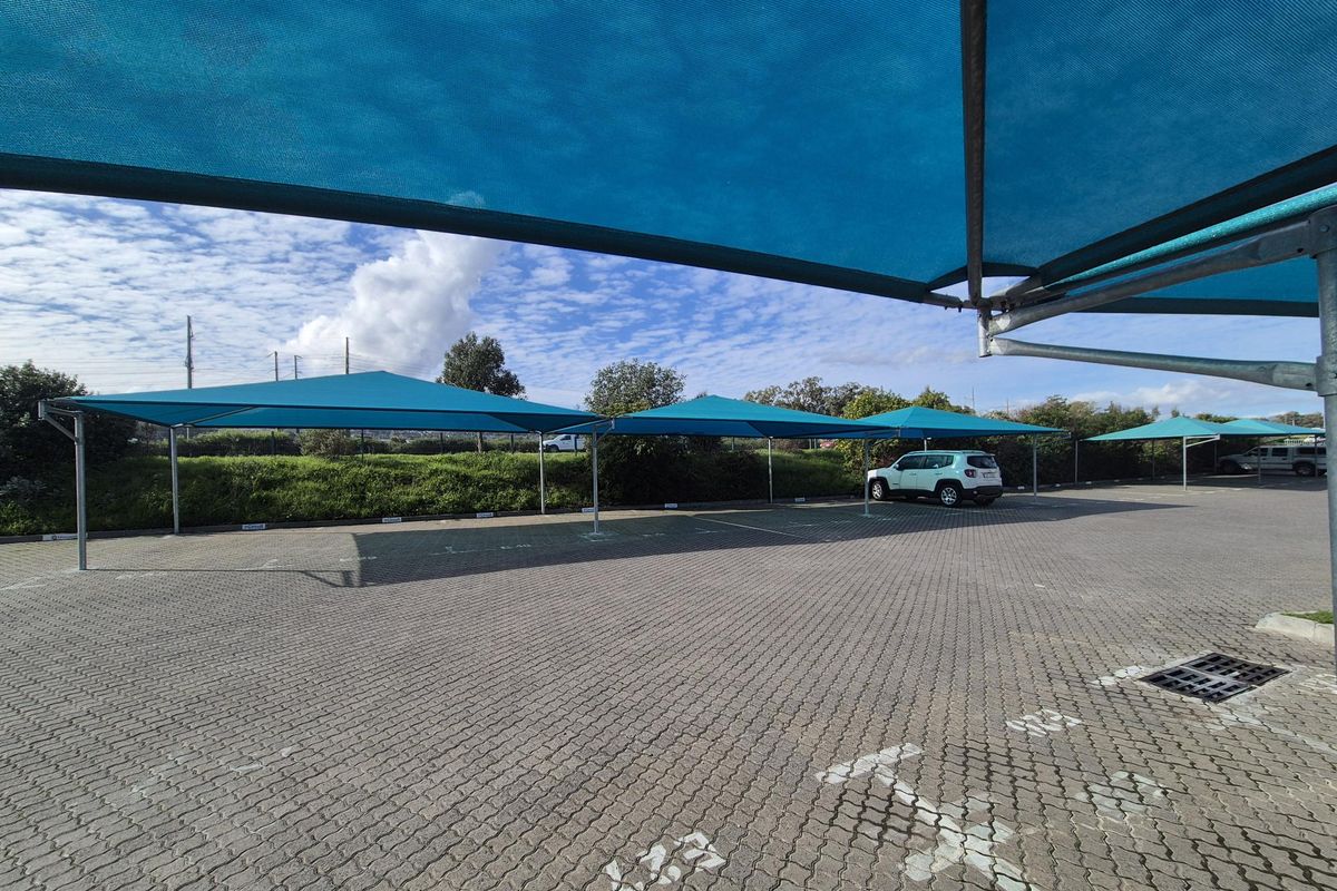 Outdoor parking area featuring paved ground and multiple blue shade cloth structures for vehicle protection.