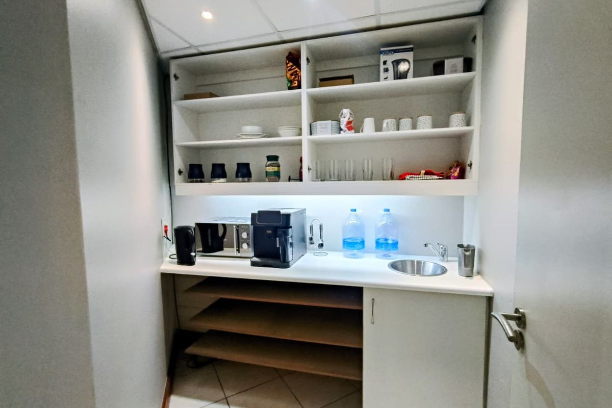 A compact office kitchenette featuring built-in cabinetry, open shelving, a small sink, and integrated under-cabinet lighting.