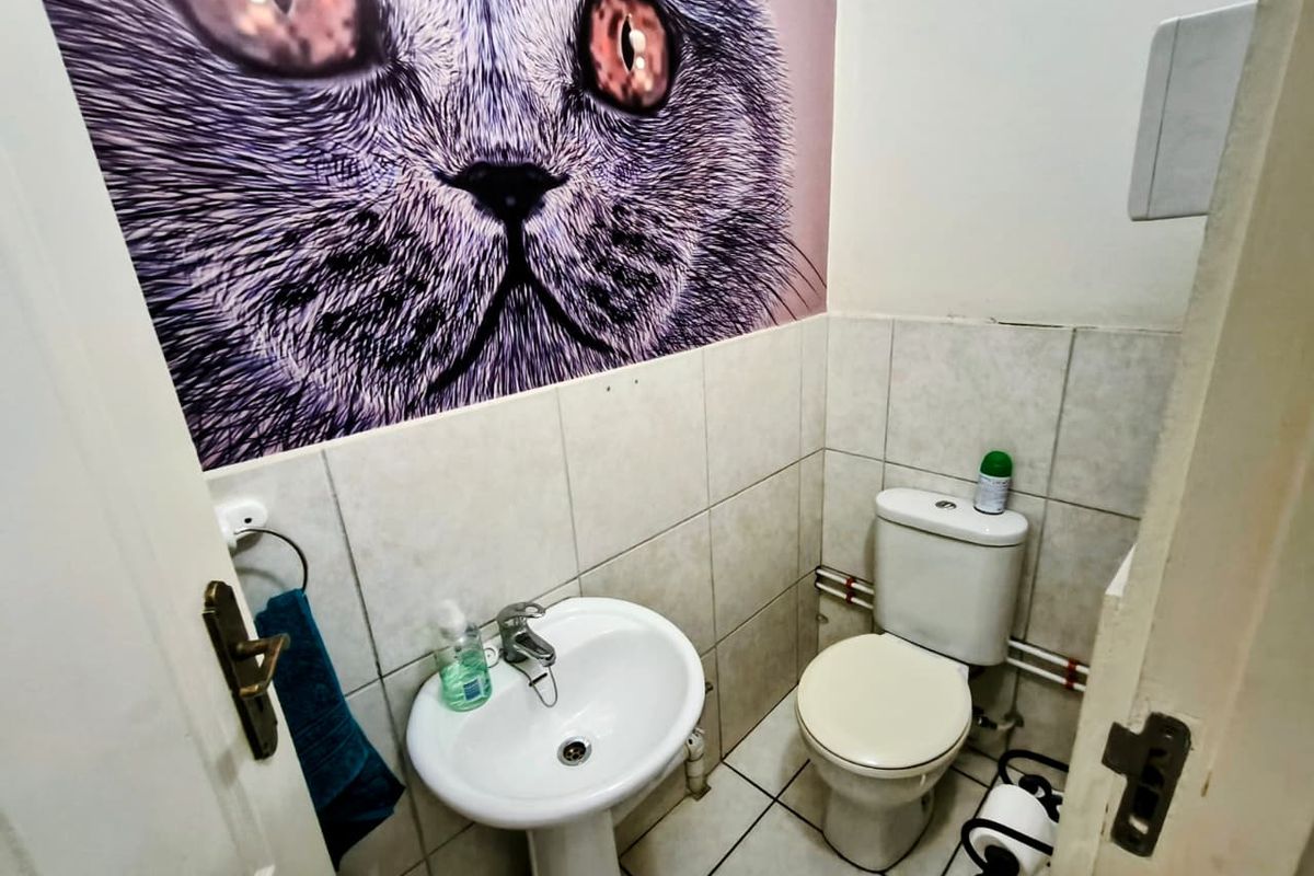 A compact office restroom featuring a pedestal sink, a standard toilet, and tiled walls with a decorative mural.