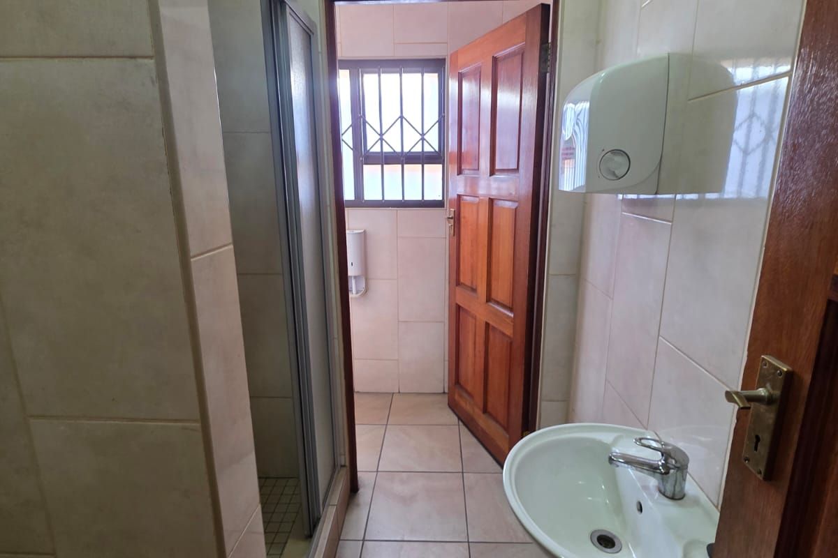 A functional bathroom featuring a pedestal sink, a shower enclosure with glass doors, and tiled walls and flooring.