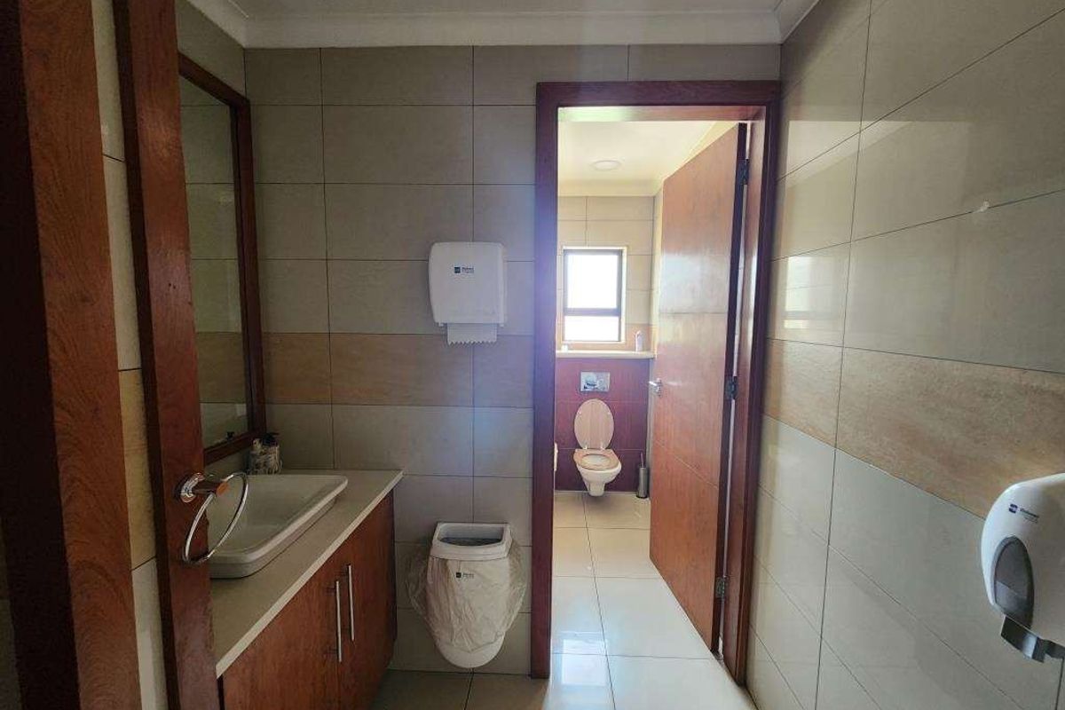 A functional commercial restroom featuring a vanity with a basin, tiled walls, and a separate toilet cubicle with a window.