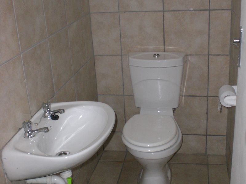 A compact bathroom featuring neutral ceramic wall and floor tiles, a wall-mounted basin, and a standard dual-flush toilet.