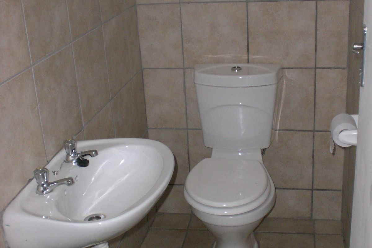 A compact bathroom featuring neutral ceramic wall and floor tiles, a wall-mounted basin, and a standard dual-flush toilet.