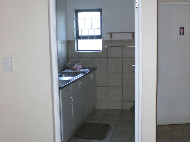 A compact kitchen area featuring built-in cabinetry, a stainless steel sink, and tiled finishes, viewed through a doorway.