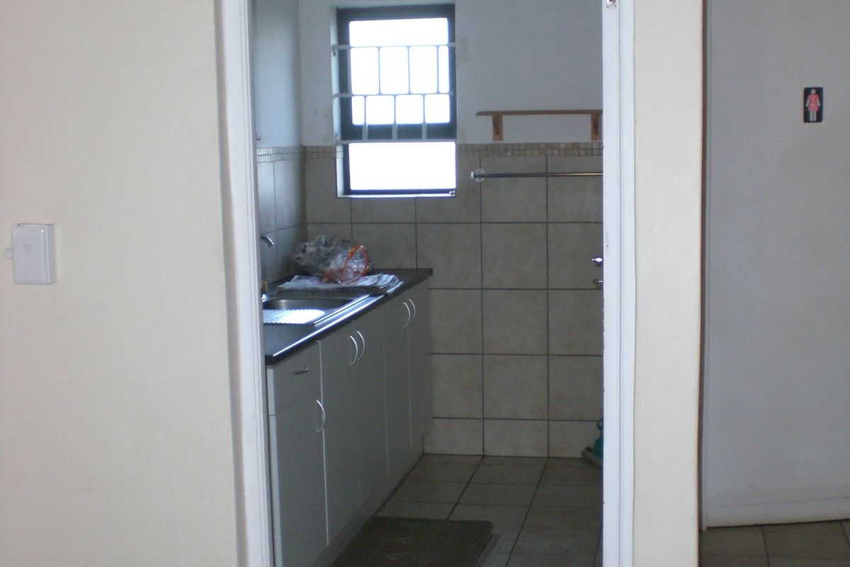 A compact kitchen area featuring built-in cabinetry, a stainless steel sink, and tiled finishes, viewed through a doorway.