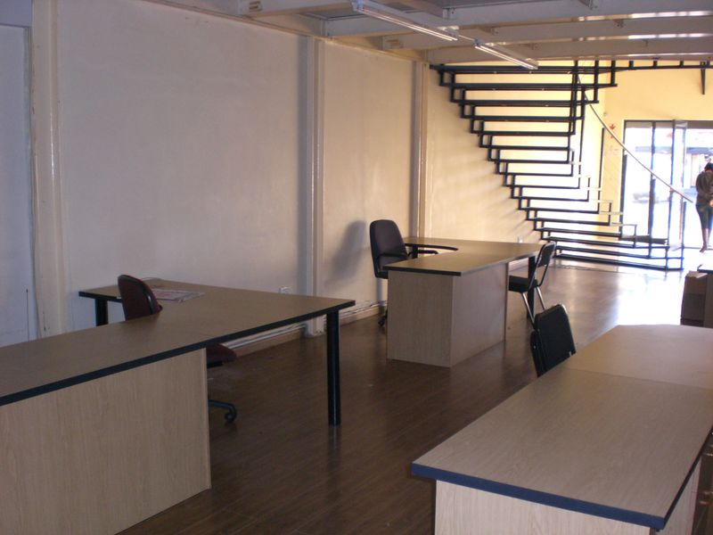Open plan retail or office space featuring laminate flooring, a prominent metal staircase, and functional overhead lighting.