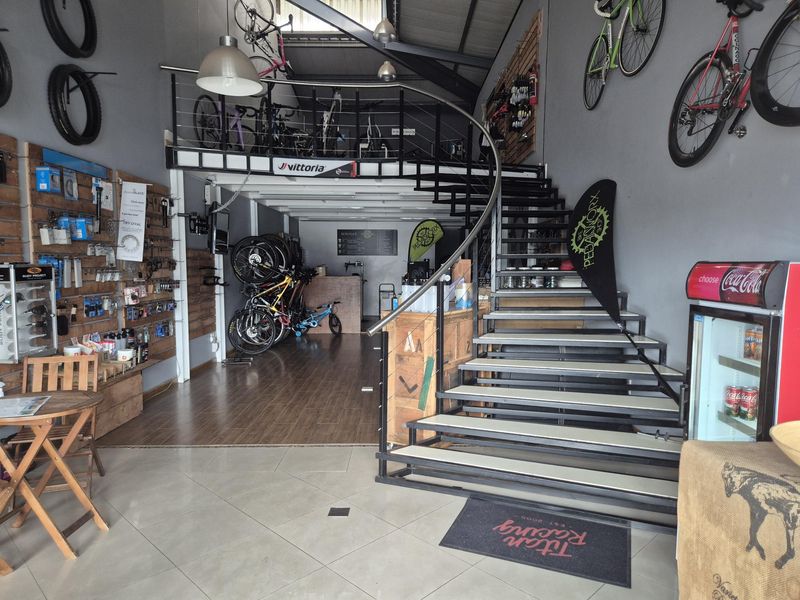 Open-plan retail space featuring a mezzanine level, metal spiral staircase, slatwall display systems, and a combination of tiled and laminate flooring.