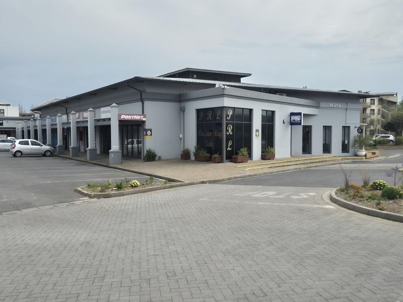 A well-maintained commercial retail building featuring a paved parking area, covered walkways, and large glass storefronts for multiple business units.