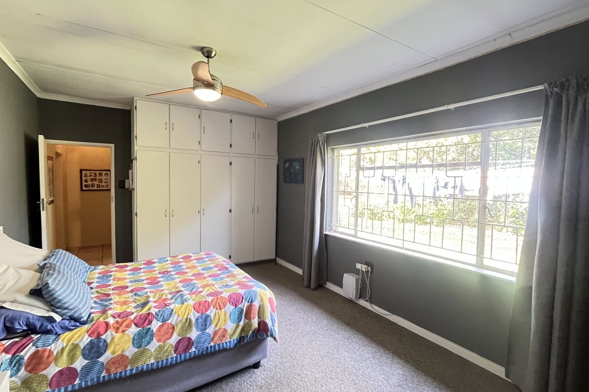 Spacious bedroom featuring built-in cupboards, large window with security bars, and neutral wall finishes.