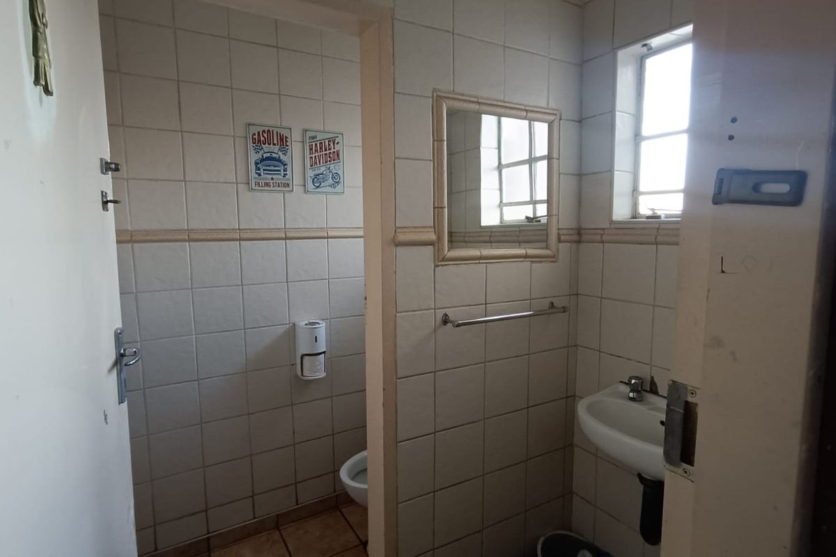 A functional, dated bathroom featuring wall-to-wall tiling, a wall-mounted basin, and a separate toilet cubicle.