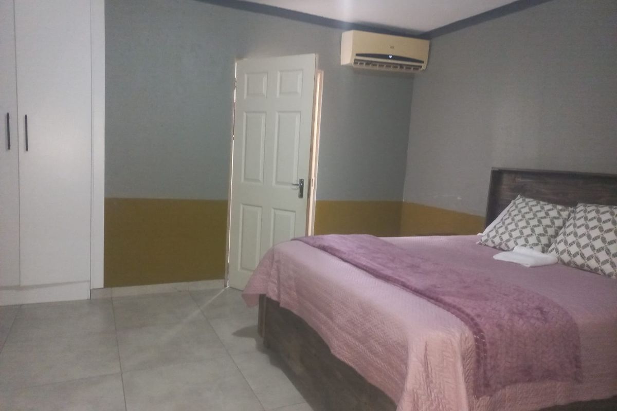 A bedroom featuring tiled flooring, built-in wardrobe cabinetry, and a wall-mounted air conditioning unit.
