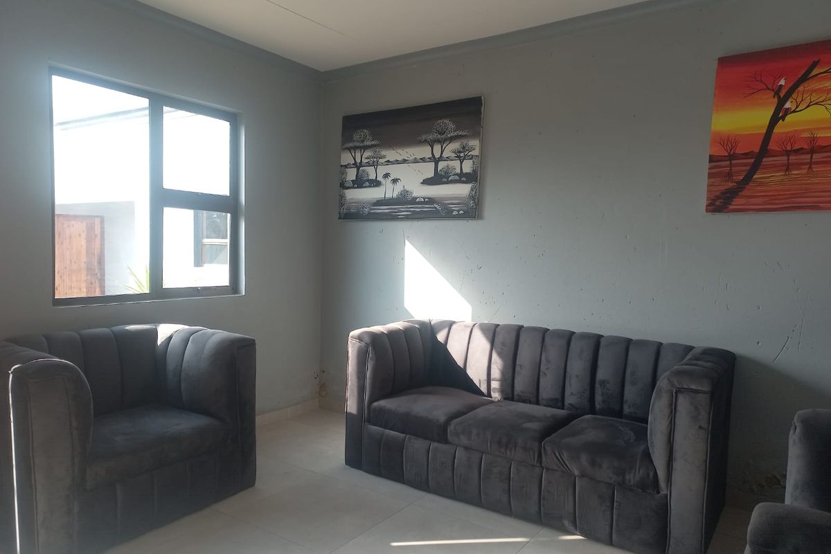 A living room area featuring tiled flooring, neutral grey walls, and natural light from a window.