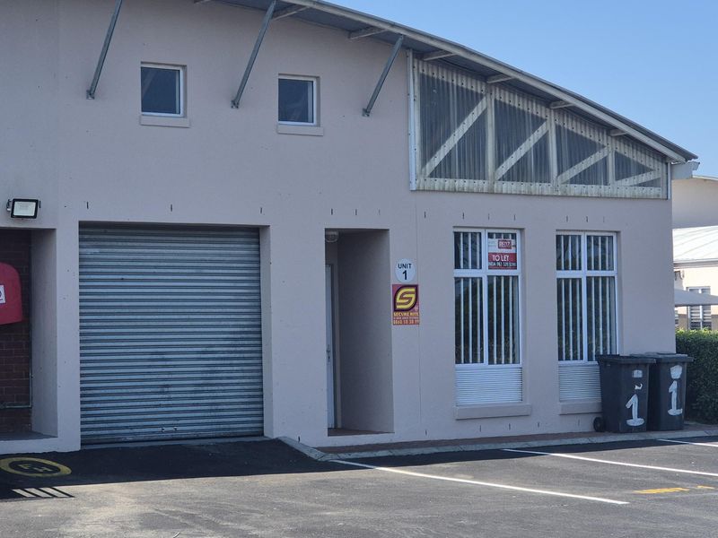 Front elevation of industrial unit featuring a roller shutter door, security-barred windows, and paved parking area.