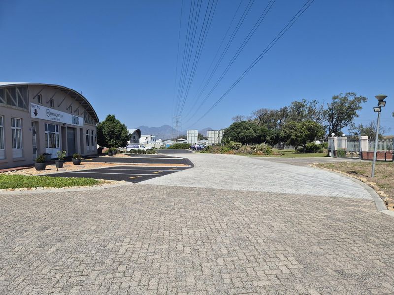 Front exterior view of an industrial unit featuring paved parking, a roller shutter door, and well-maintained surrounding grounds.