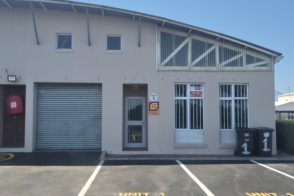 Front elevation of an industrial unit featuring a roller shutter door, pedestrian entrance with security gate, and dedicated asphalt parking bay.