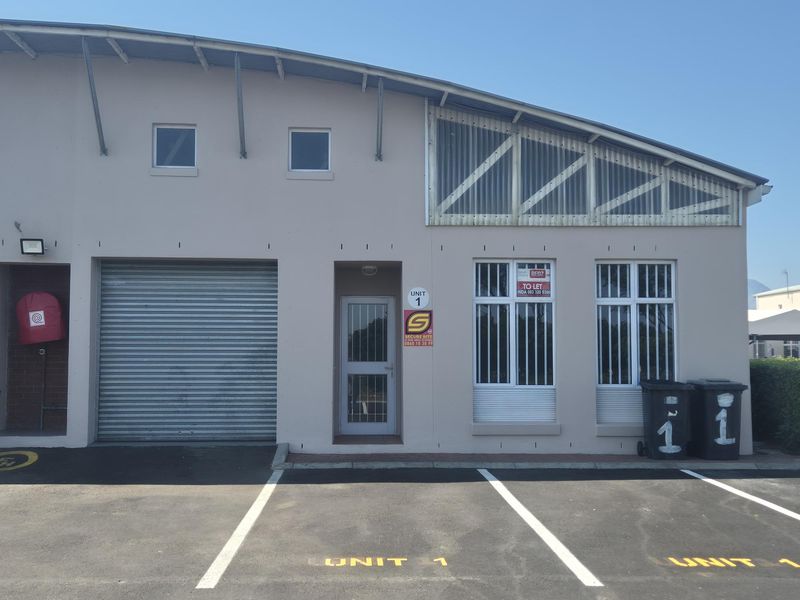 Front elevation of an industrial unit featuring a roller shutter door, pedestrian entrance with security gate, and dedicated asphalt parking bay.