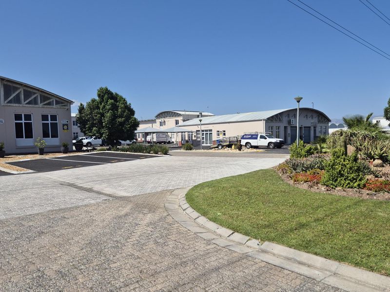 A well-maintained industrial park exterior featuring paved parking areas, landscaped garden beds, and modern industrial building facades under a clear sky.