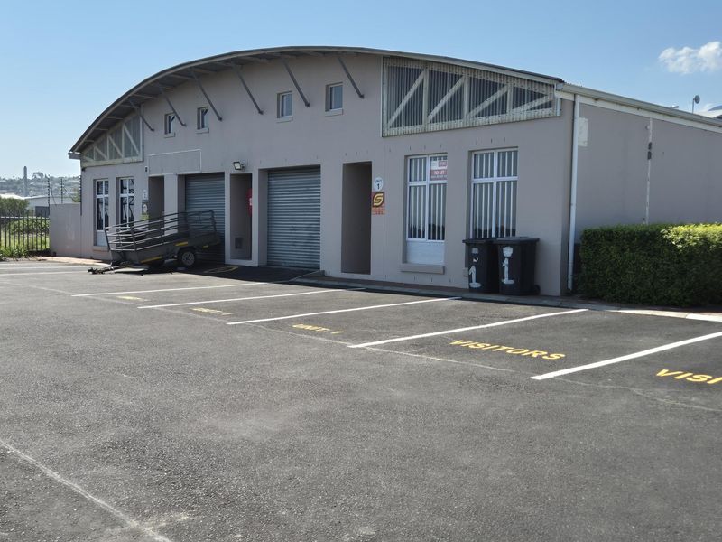 Front view of an industrial unit featuring a curved roof, roller shutter doors, and dedicated asphalt parking spaces.