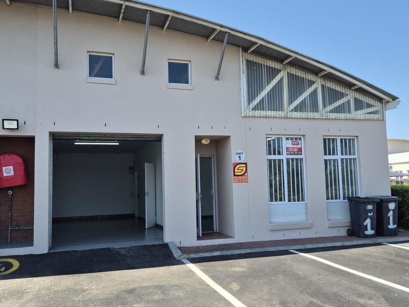 Front elevation of an industrial unit featuring a roller shutter door, pedestrian entrance, security bars, and dedicated asphalt parking space.