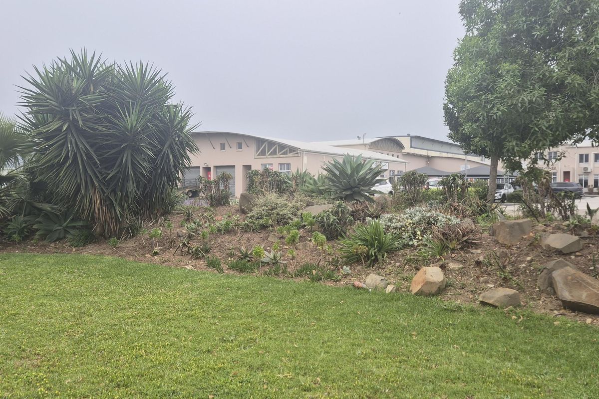 View of the industrial property exterior featuring a landscaped garden area and curved roof architecture with roller door access.
