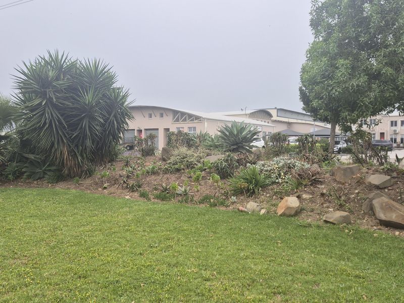 View of the industrial property exterior featuring a landscaped garden area and curved roof architecture with roller door access.
