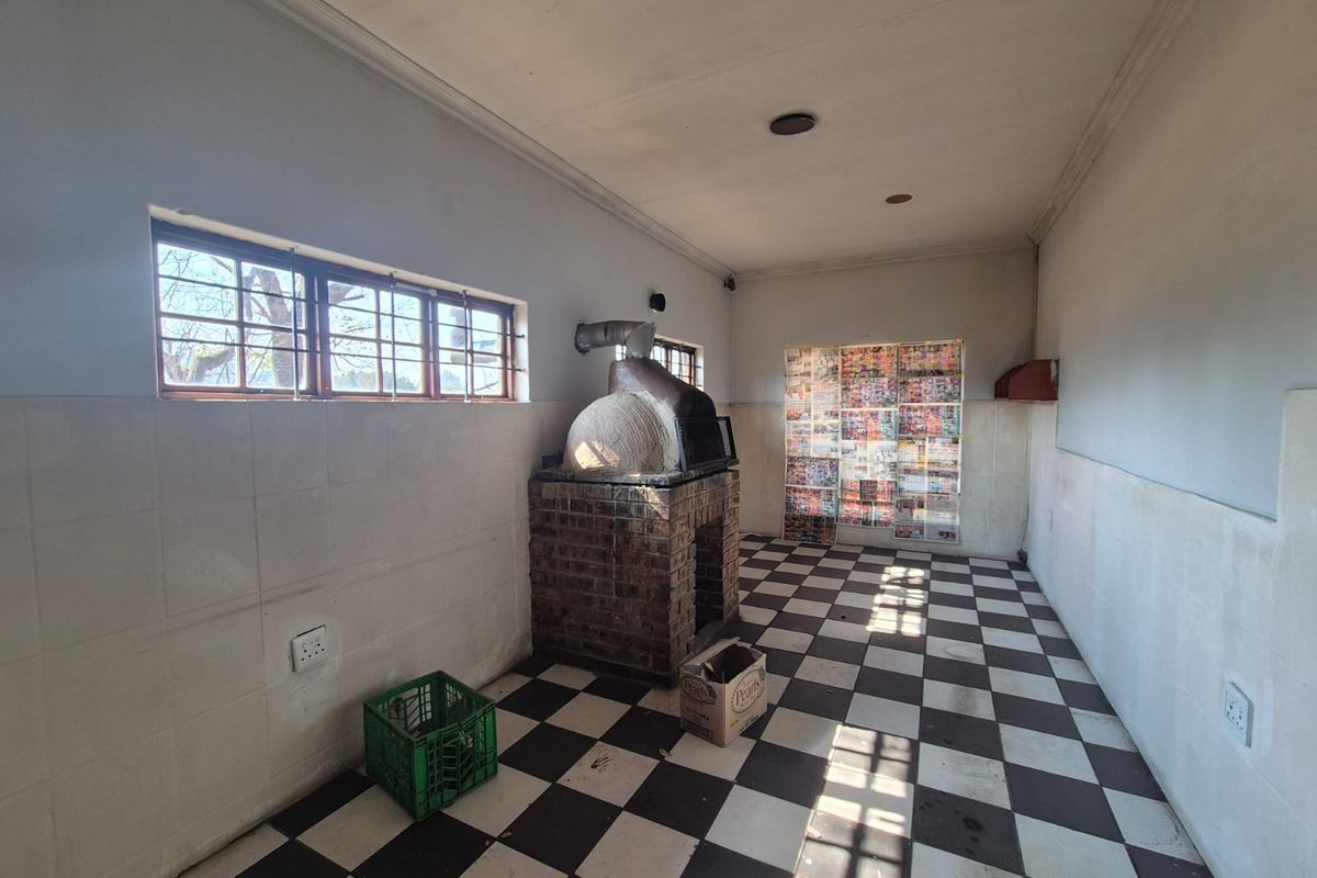 A functional kitchen area featuring a built-in brick pizza oven, checkered floor tiling, and wall-mounted tiled splashbacks.