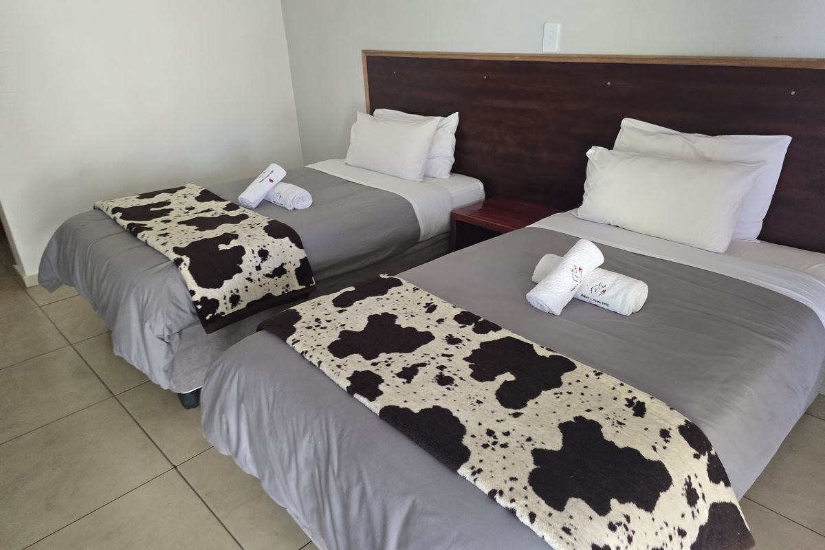 A hotel bedroom featuring a built-in dark wood headboard and neutral floor tiling.