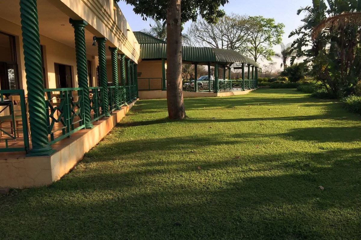 Spacious hotel grounds featuring a long covered veranda with decorative green columns and a well-maintained lawn area.