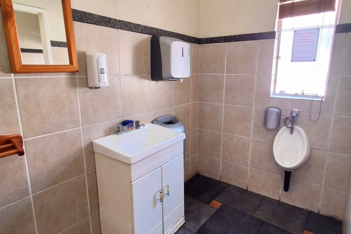 A functional office restroom featuring a vanity basin, wall-mounted urinal, and tiled finishes throughout.