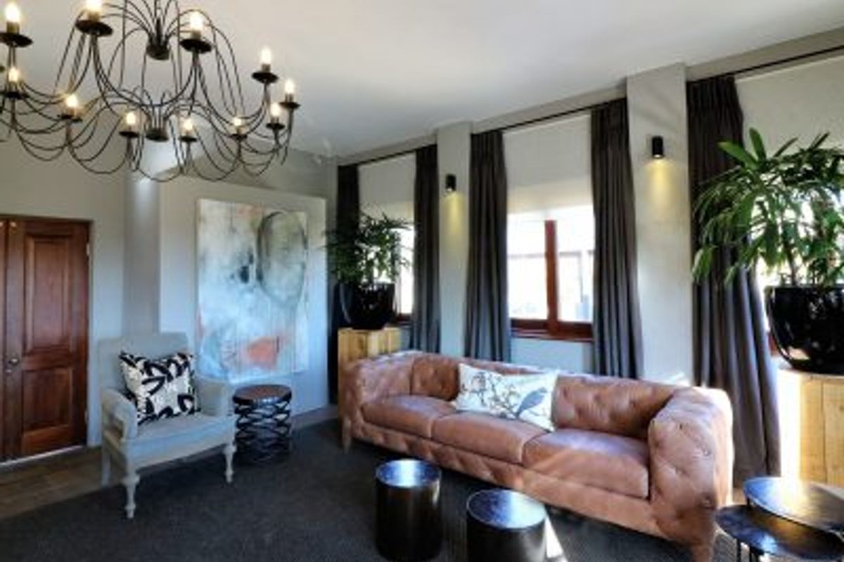 A well-appointed hotel lounge area featuring a decorative chandelier, recessed wall lighting, and large windows with floor-to-ceiling curtains.