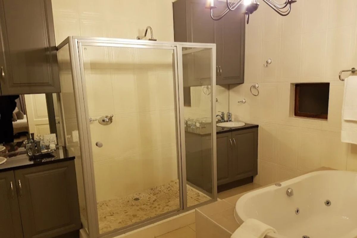 A well-appointed hotel bathroom featuring a glass-enclosed shower, a built-in jetted bathtub, and dark cabinetry with integrated vanity sinks.