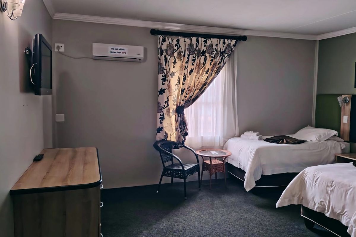 A hotel bedroom featuring two beds, wall-mounted air conditioning unit, and neutral wall finishes.