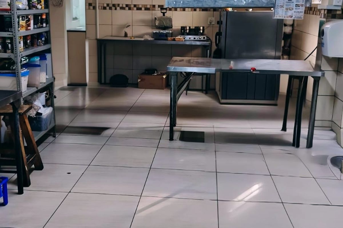 A functional commercial kitchen space featuring tiled walls and flooring, stainless steel prep tables, and a mounted extractor hood.