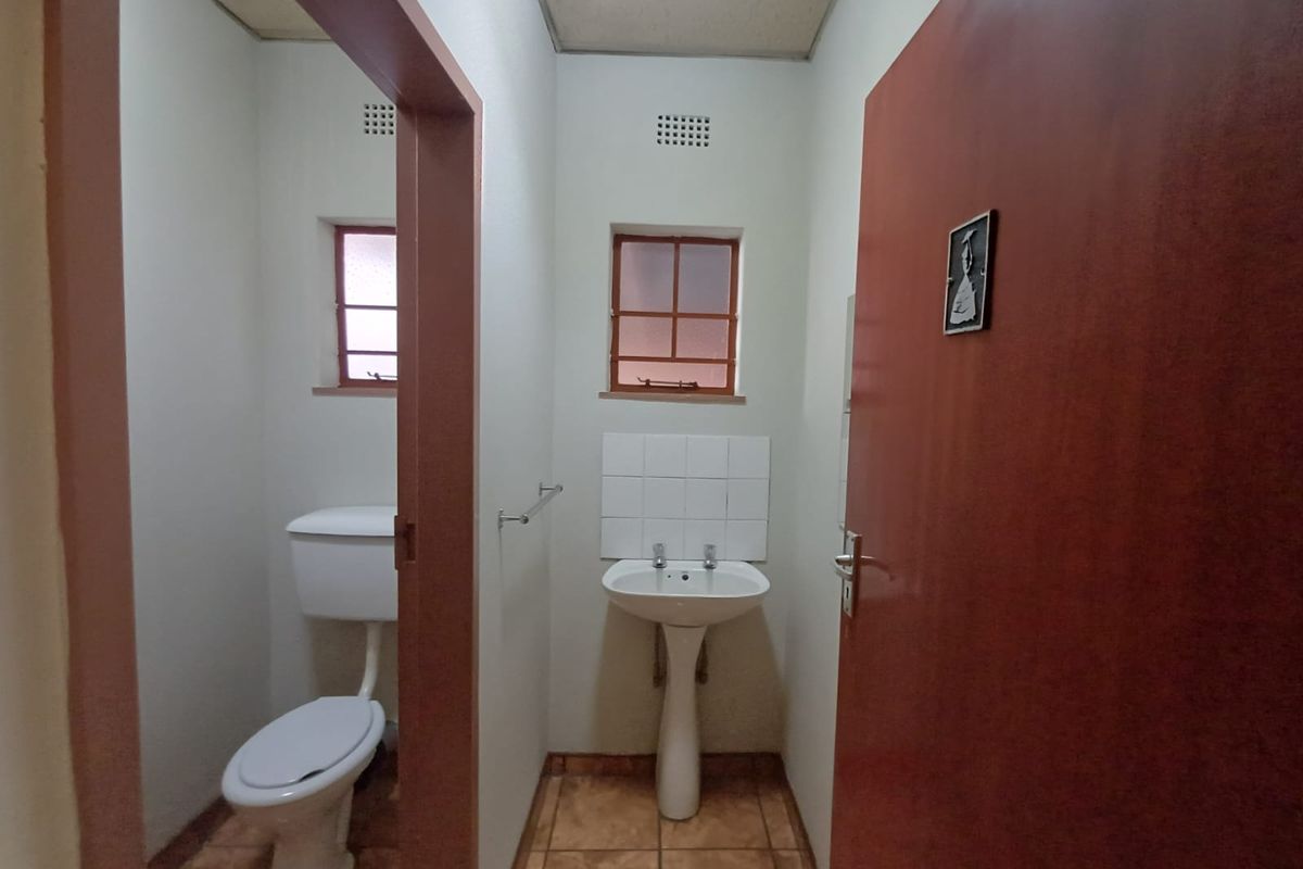 A functional industrial restroom featuring a pedestal basin with tiled splashback and a separate toilet cubicle with natural ventilation.