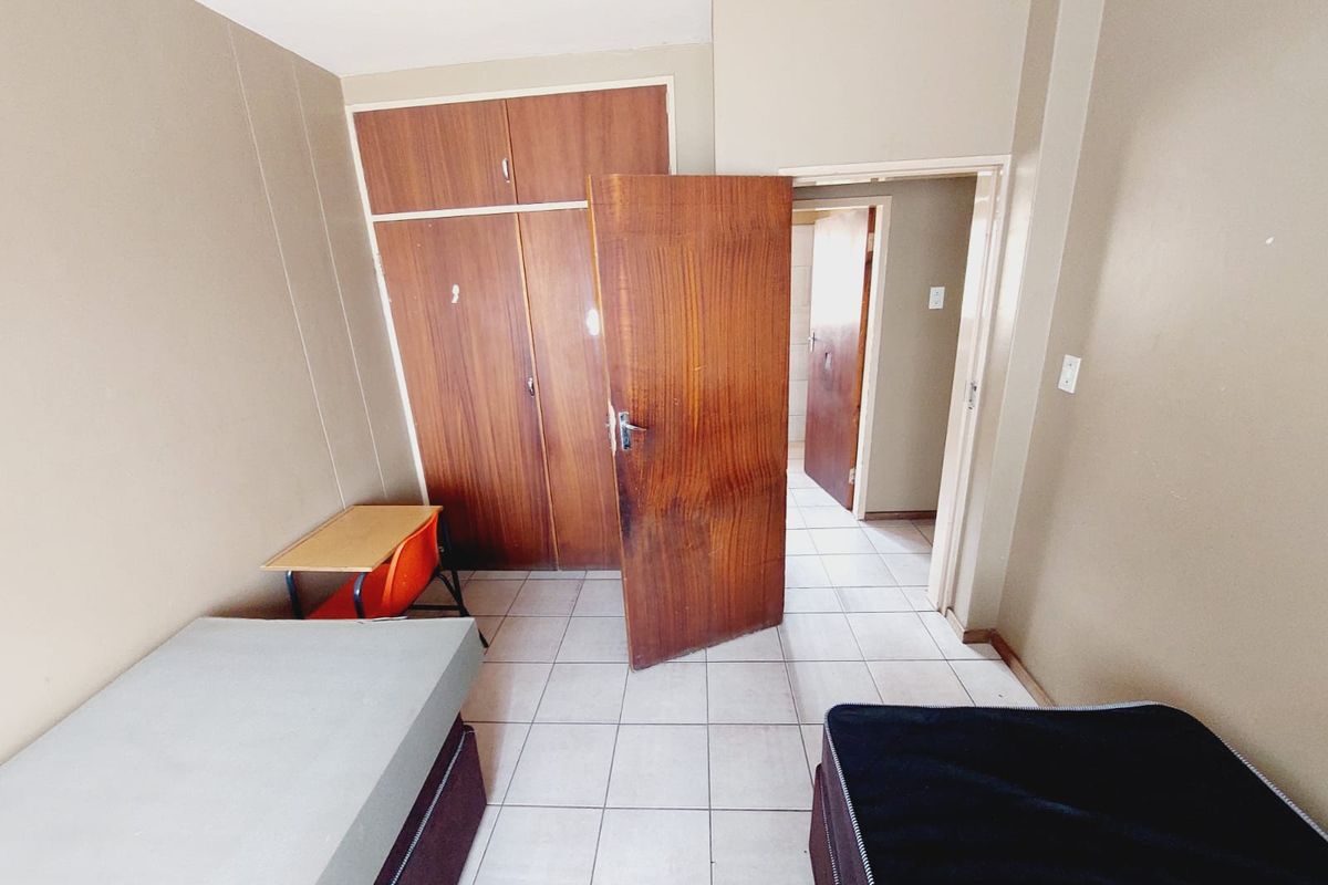 A bedroom featuring built-in wooden cupboards, tiled flooring, and direct access to an adjoining hallway.