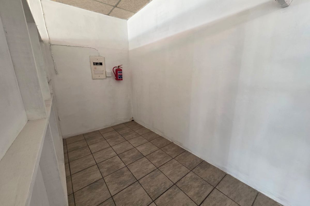 A functional, empty utility space featuring tiled flooring, built-in shelving, and essential safety equipment including a fire extinguisher and electrical distribution board.