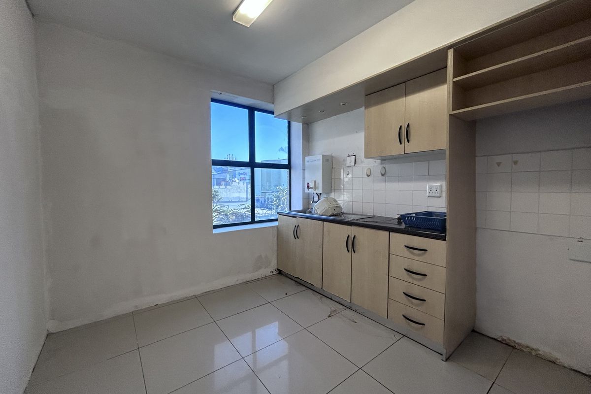A functional office kitchenette featuring light wood cabinetry, tiled backsplash, a stainless steel sink, and a wall-mounted water heater.