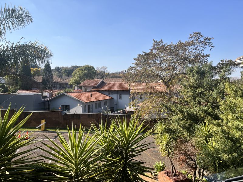 An elevated view overlooking a paved parking area, surrounding residential buildings with tiled roofs, and established garden greenery.