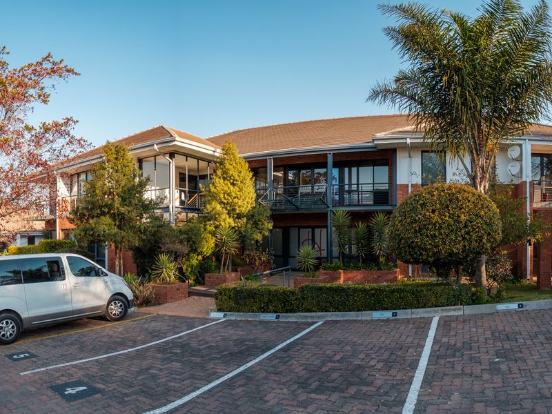 A well-maintained two-story office building featuring brick facade, balconies, and an adjacent paved parking area with established landscaping.