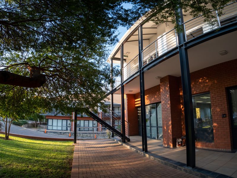 A modern office building exterior featuring exposed brickwork, steel structural elements, and a covered balcony area with paved walkways.