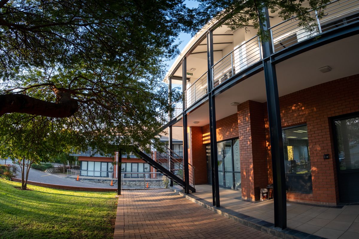 A modern office building exterior featuring exposed brickwork, steel structural elements, and a covered balcony area with paved walkways.