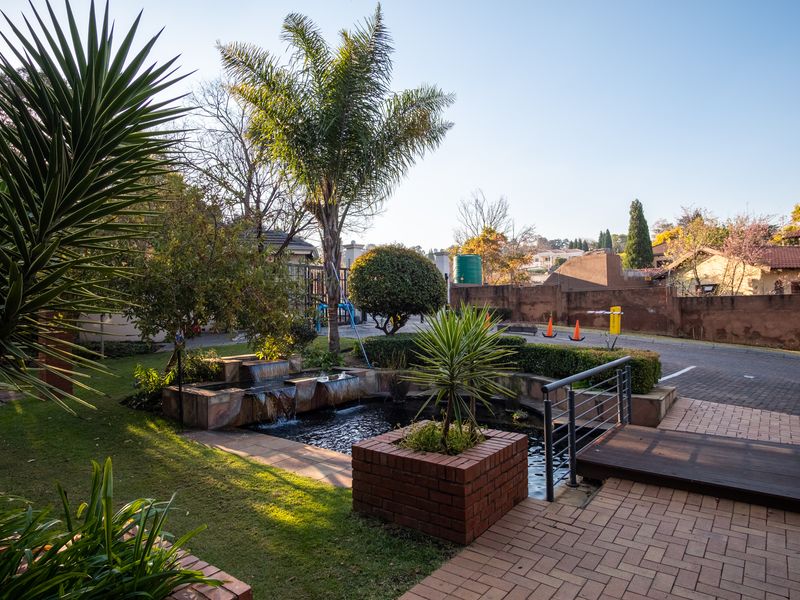Front exterior view featuring a landscaped garden, a tiered water feature, brick planters, and a paved entrance area with timber decking.