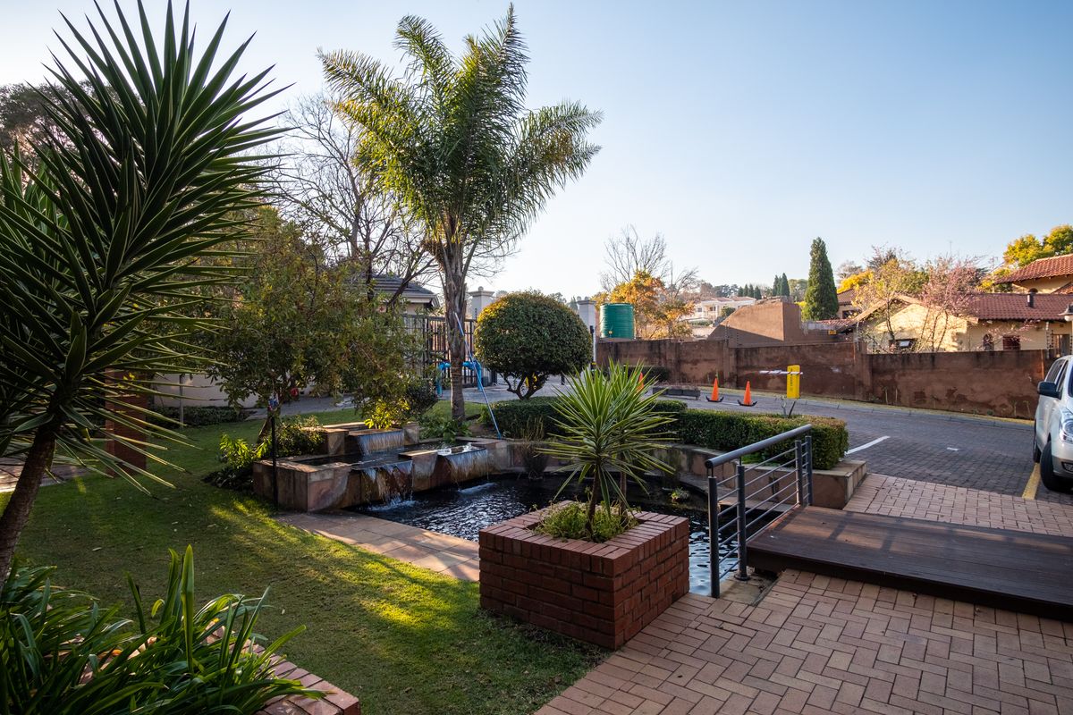 Front exterior view featuring a landscaped garden, a tiered water feature, brick planters, and a paved entrance area with timber decking.