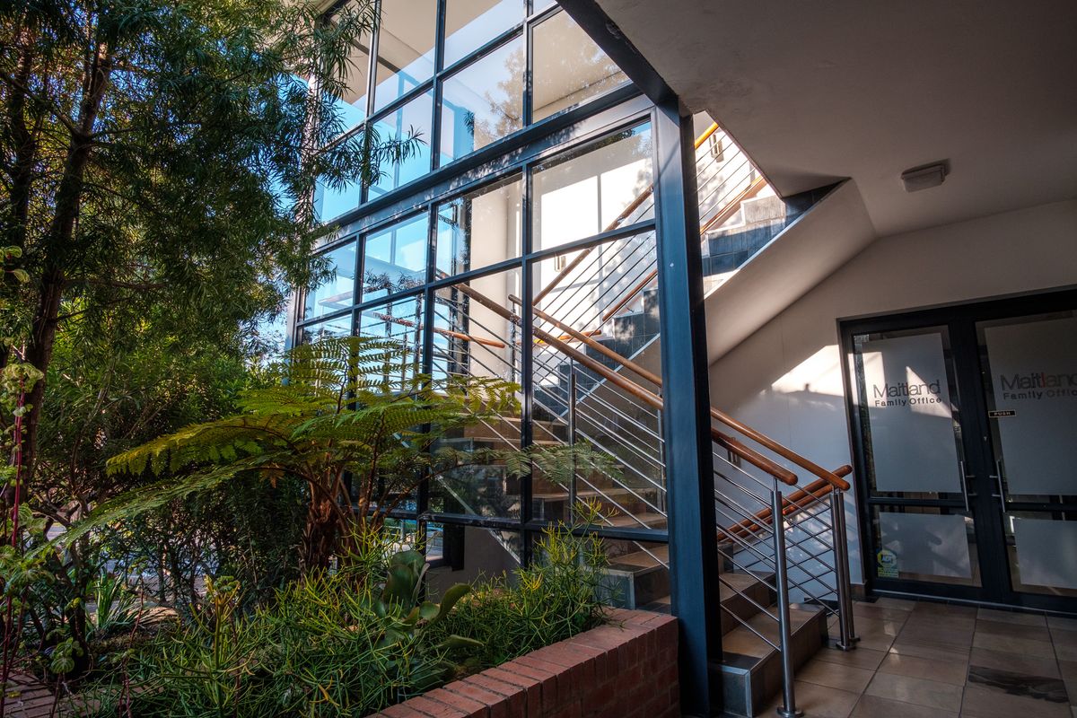 Modern office entrance featuring a striking full-height glass facade, steel staircase with timber handrails, and a landscaped brick planter box.