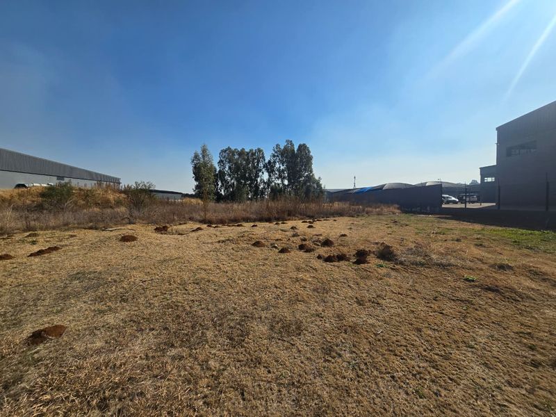 A view of a vacant commercial land plot with dry grass and surrounding industrial structures.