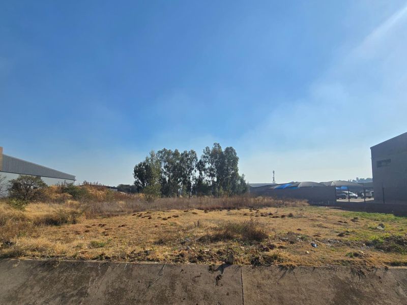 A view of a vacant commercial land plot featuring a concrete retaining wall and surrounding industrial development.