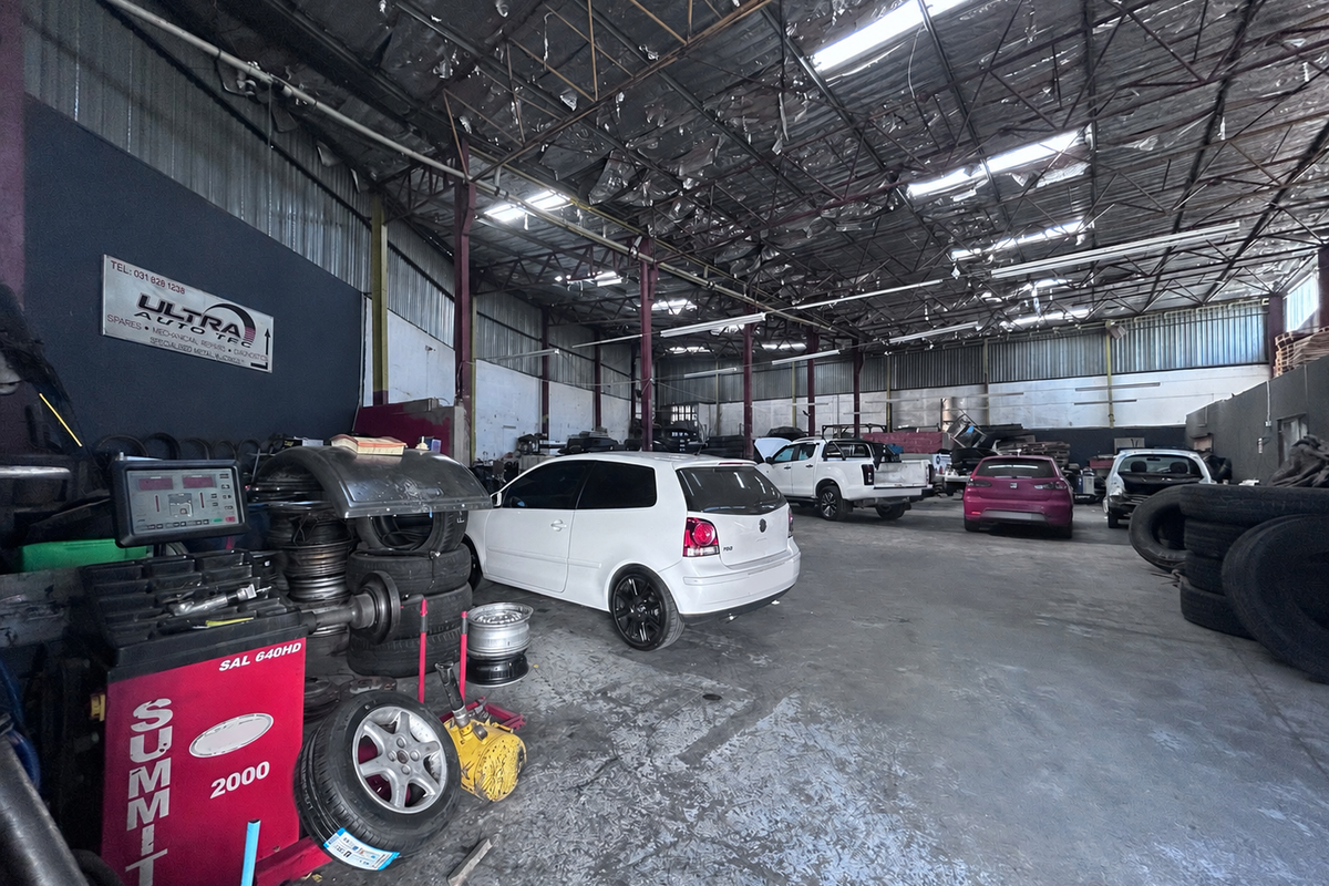 Spacious industrial workshop featuring high exposed steel roof trusses, concrete flooring, and functional lighting, suitable for automotive repair or storage operations.