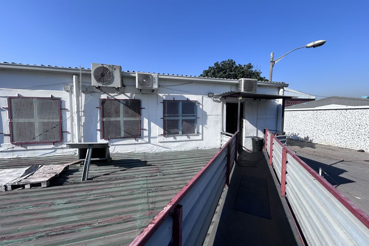 Rear exterior view of the industrial building featuring a metal access ramp, security window grilles, and external air conditioning units.