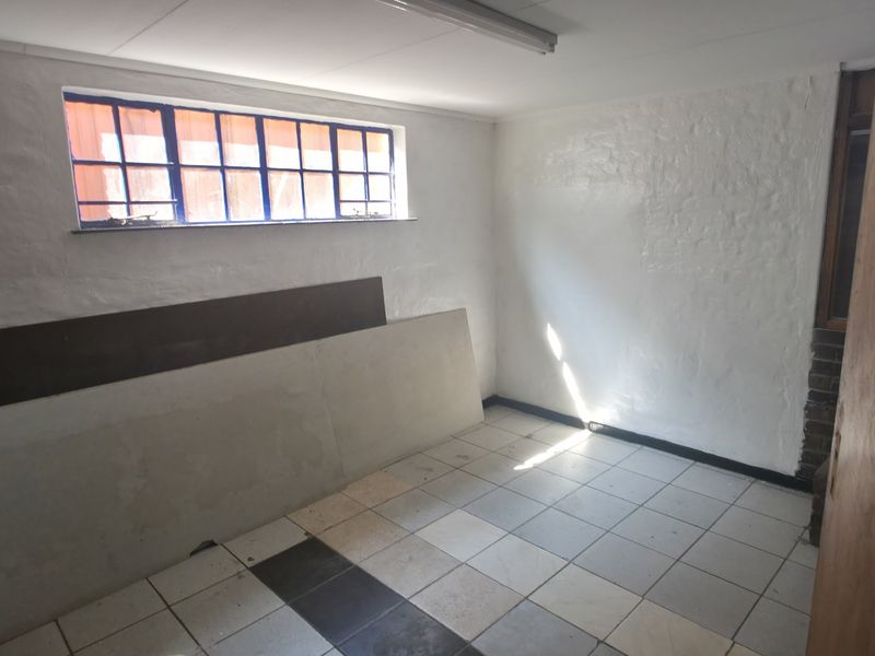 A vacant utility space featuring tiled flooring, security bars on the window, and basic overhead lighting, suitable for storage or workshop use.